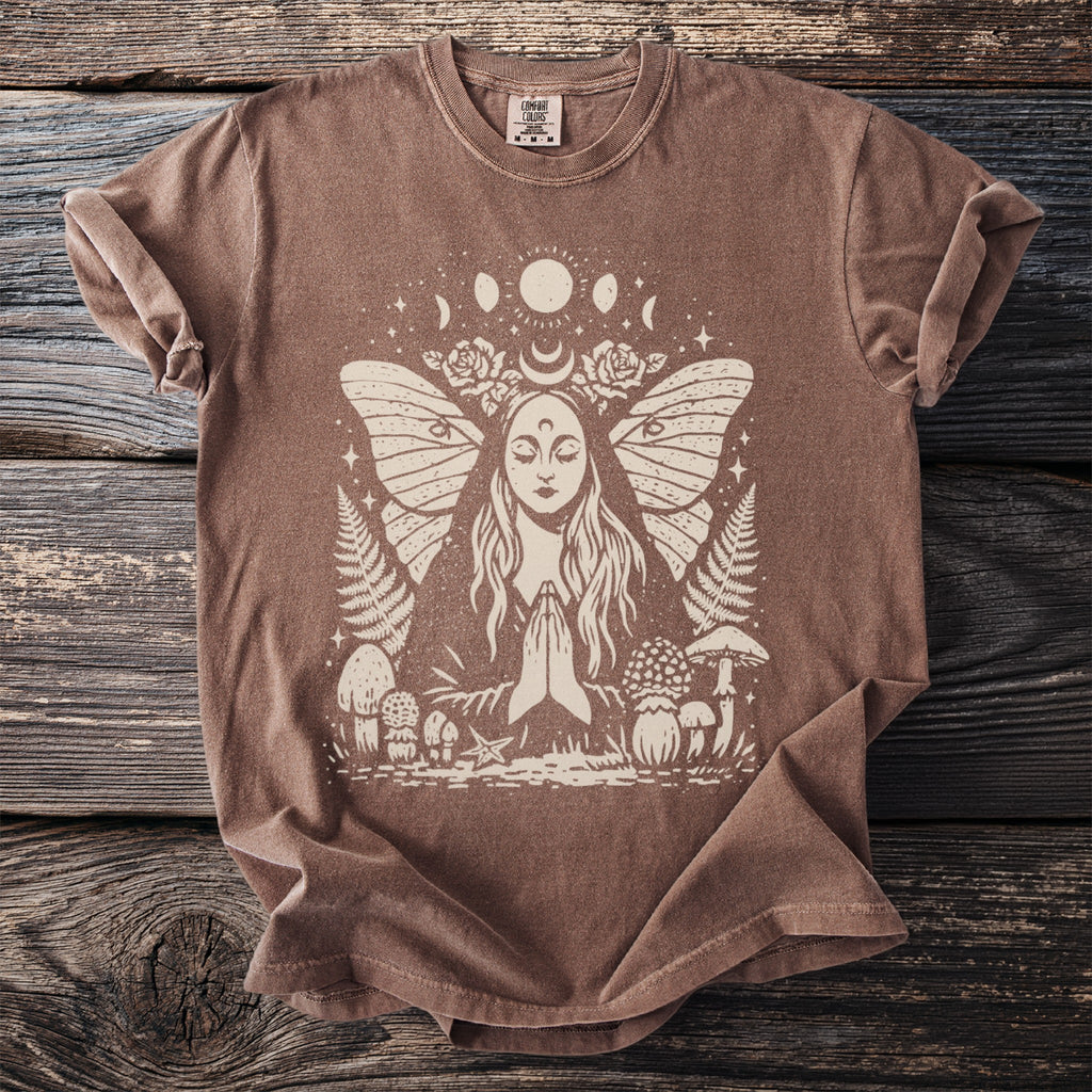Brown t-shirt with cream graphic of praying woman surrounded by moths, moons, mushrooms, and ferns.