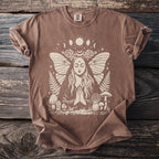 Brown t-shirt with cream graphic of praying woman surrounded by moths, moons, mushrooms, and ferns.