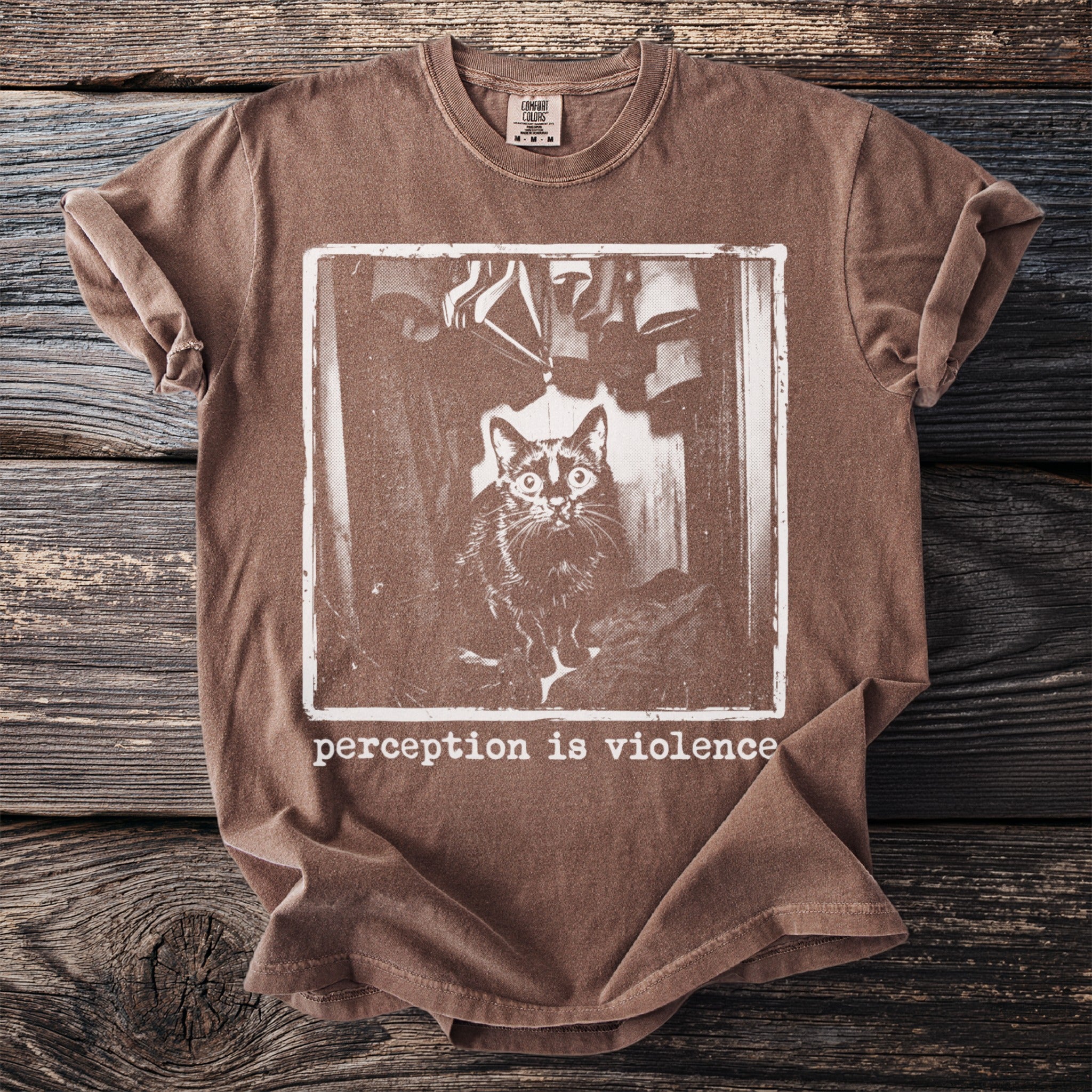 Brown t-shirt with framed graphic of cat in closet and text "perception is violence".