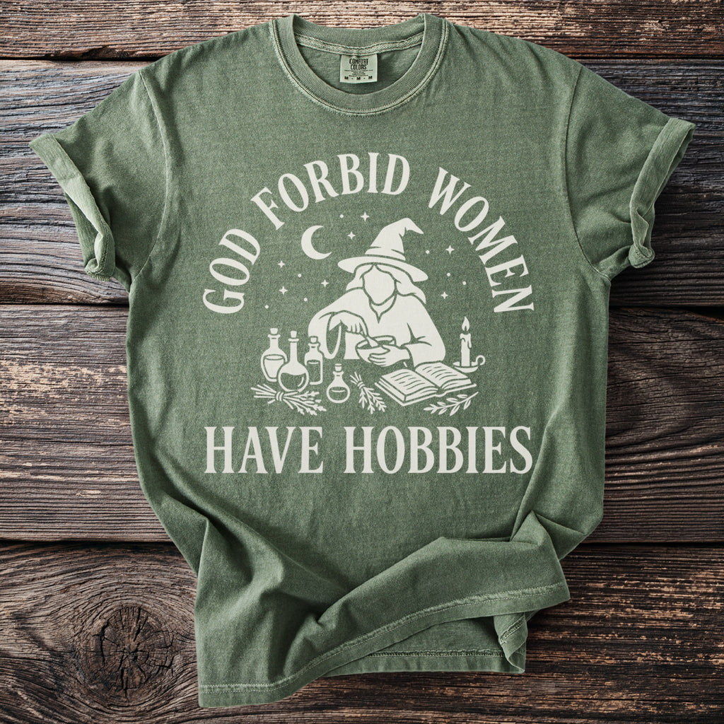Green t-shirt with "God Forbid Women Have Hobbies" text and witch graphic.