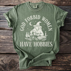 Green t-shirt with "God Forbid Women Have Hobbies" text and witch graphic.