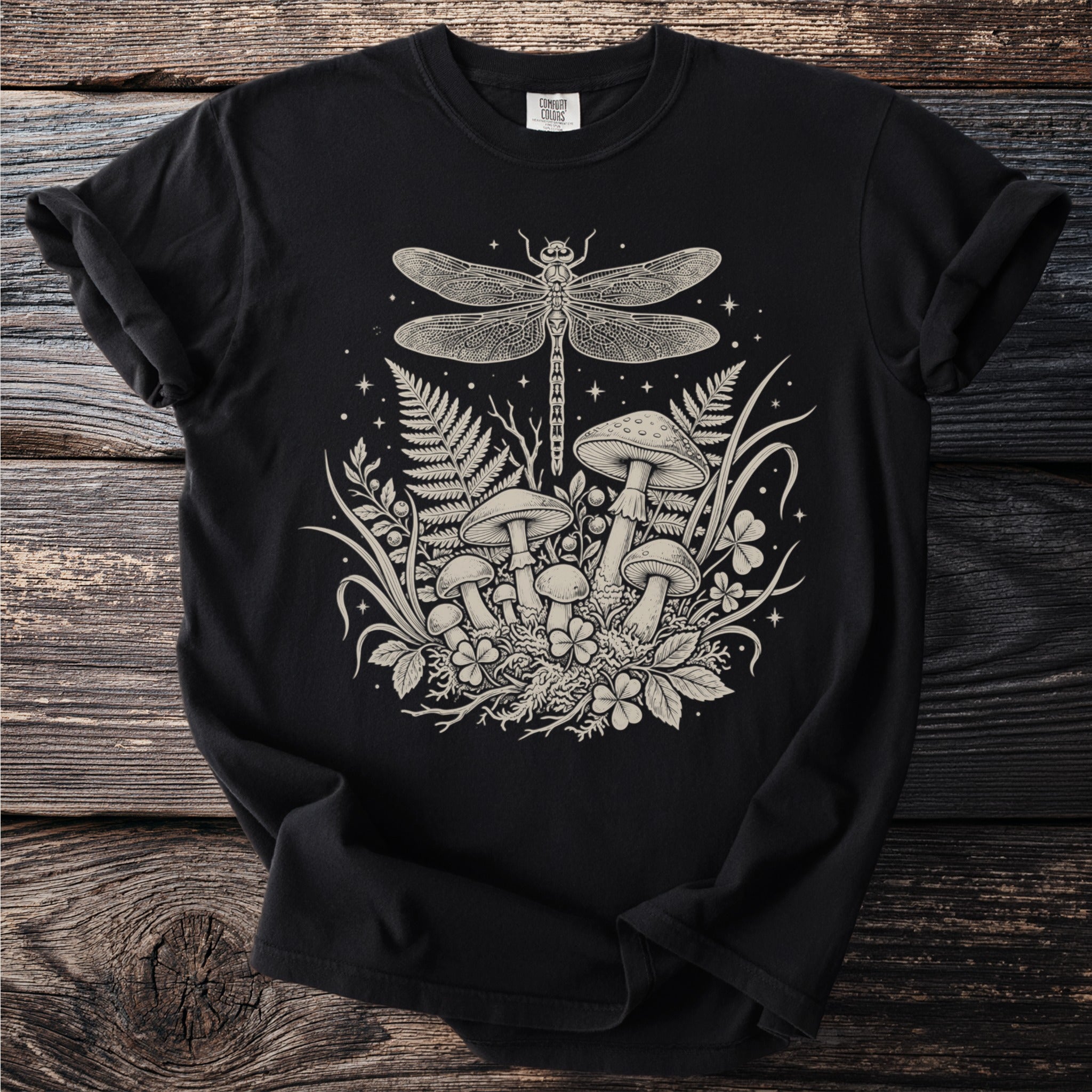 Black t-shirt with a cream linework design of a dragonfly over mushrooms and ferns.
