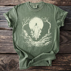 Green t-shirt with a light-colored hooded figure and trees framing a moon.