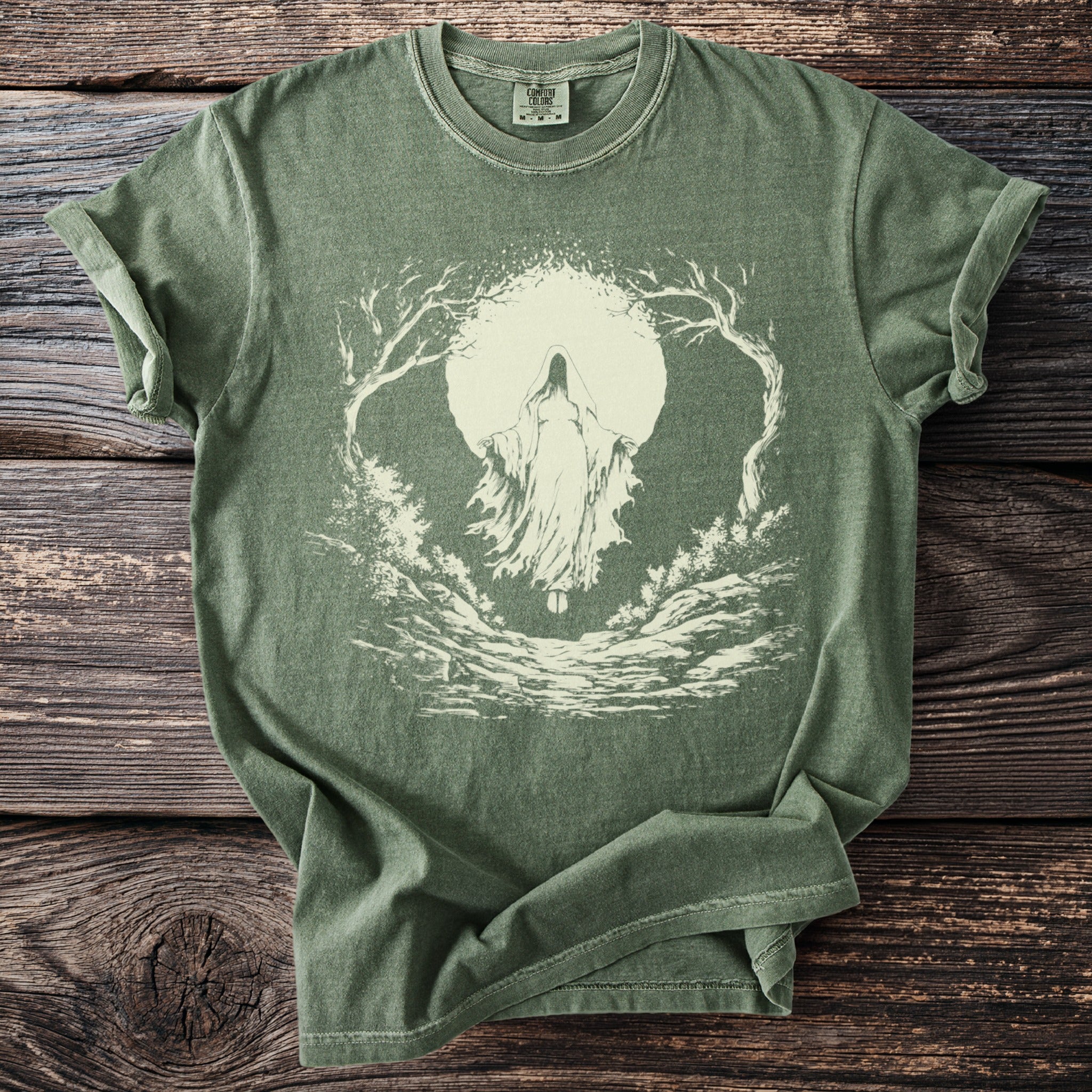Green t-shirt with a light-colored hooded figure and trees framing a moon.