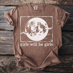 Brown t-shirt with witches flying on broomsticks before a full moon and the text "girls will be girls".