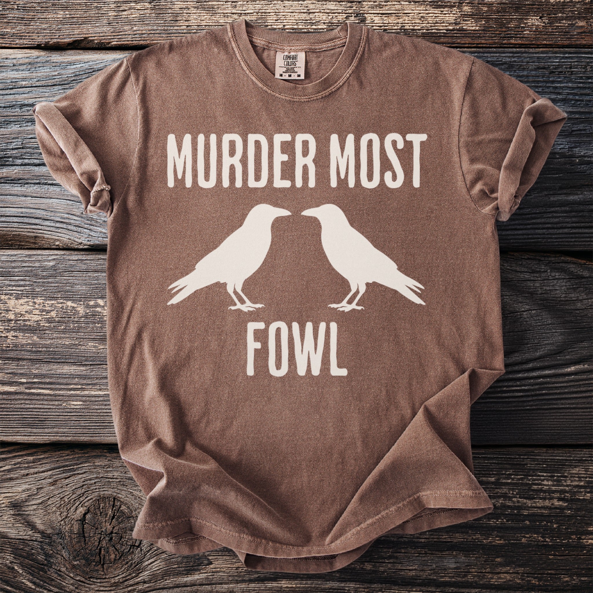 Brown t-shirt with "MURDER MOST FOWL" and two white birds.