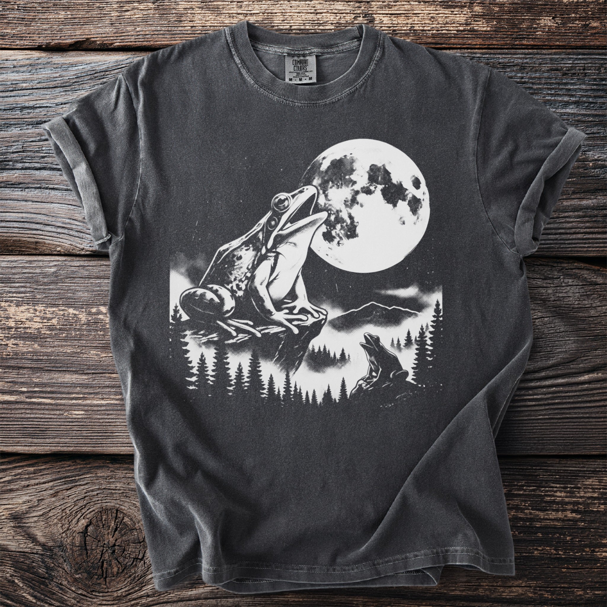 T-shirt with graphic of frogs and moon in a forest landscape.