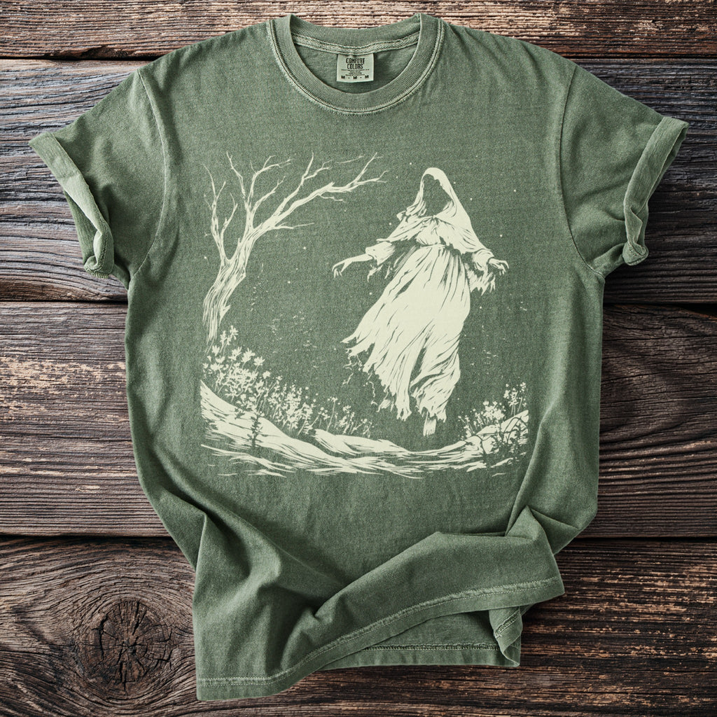 Green t-shirt with faded ghost and tree graphic centered on distressed wood.