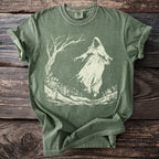 Green t-shirt with faded ghost and tree graphic centered on distressed wood.