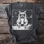 Graphic t-shirt with a black and white raccoon wearing sunglasses and drinking from a cup.