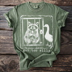 Green t-shirt with a distressed graphic of a raccoon holding a spoon in a cage and a goose outside.