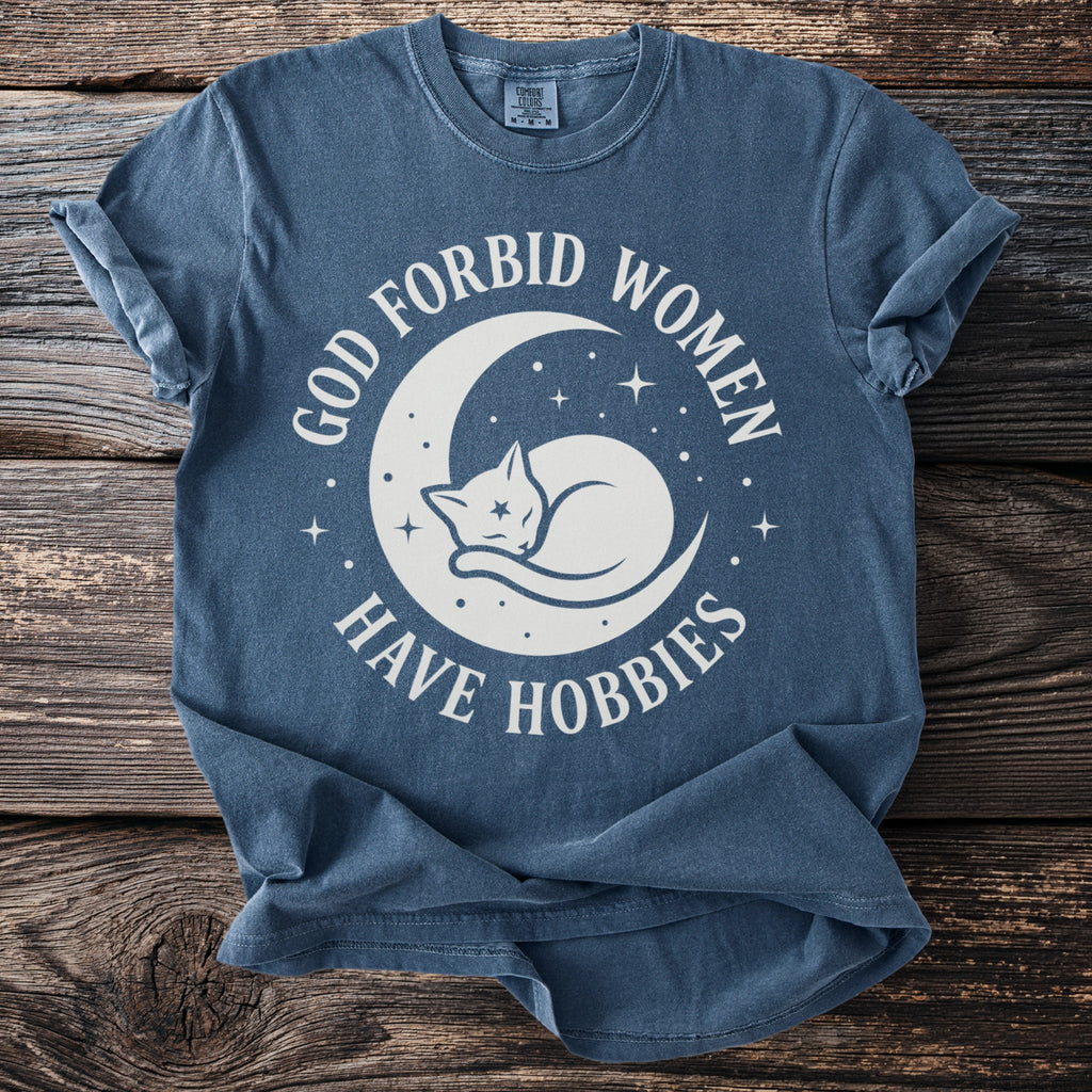 Blue t-shirt with white text and graphic: "God forbid women have hobbies" and a sleeping cat on the moon.