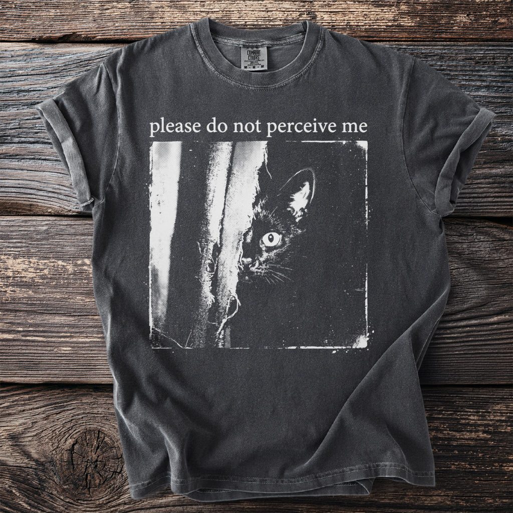 Dark t-shirt with a black cat peeking from behind a tree and text "please do not perceive me".
