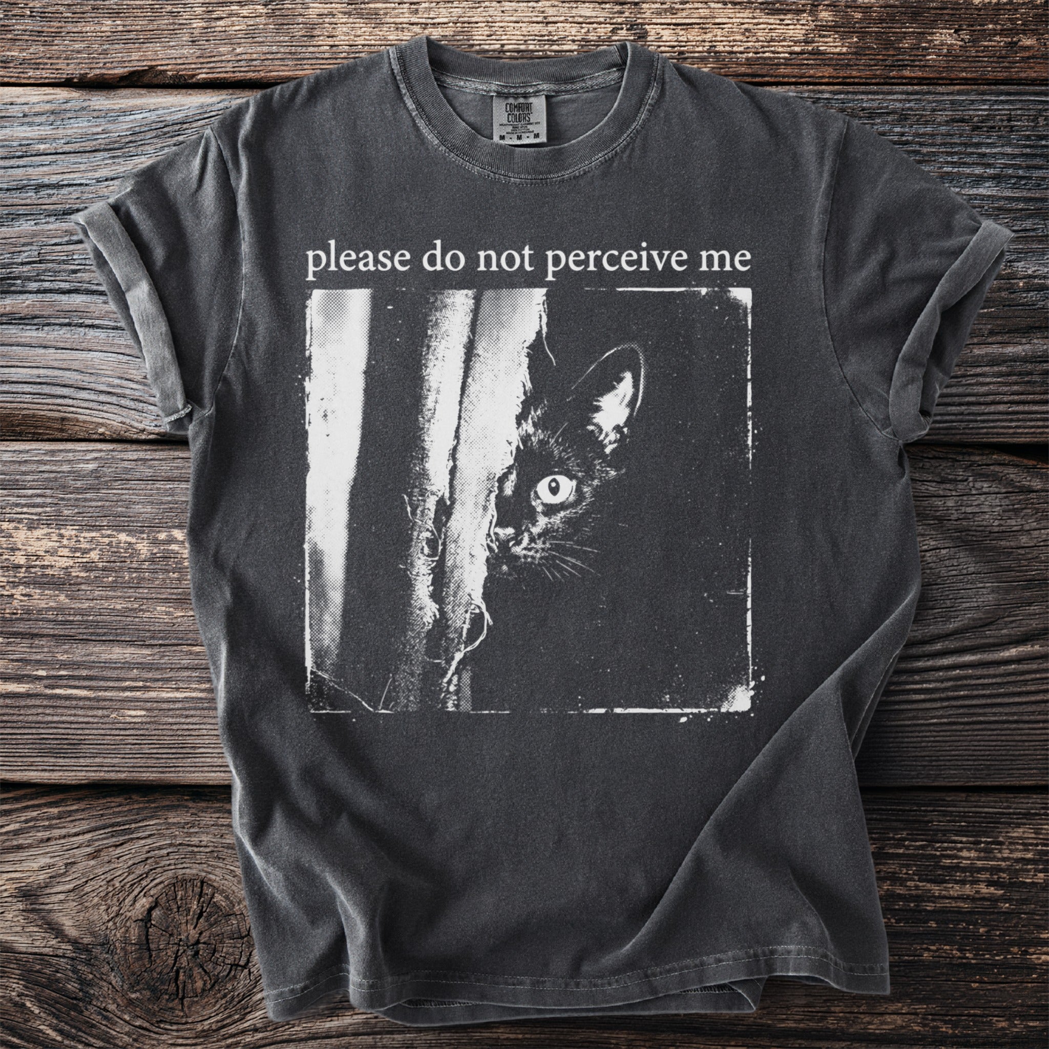 Dark t-shirt with a black cat peeking from behind a tree and text "please do not perceive me".