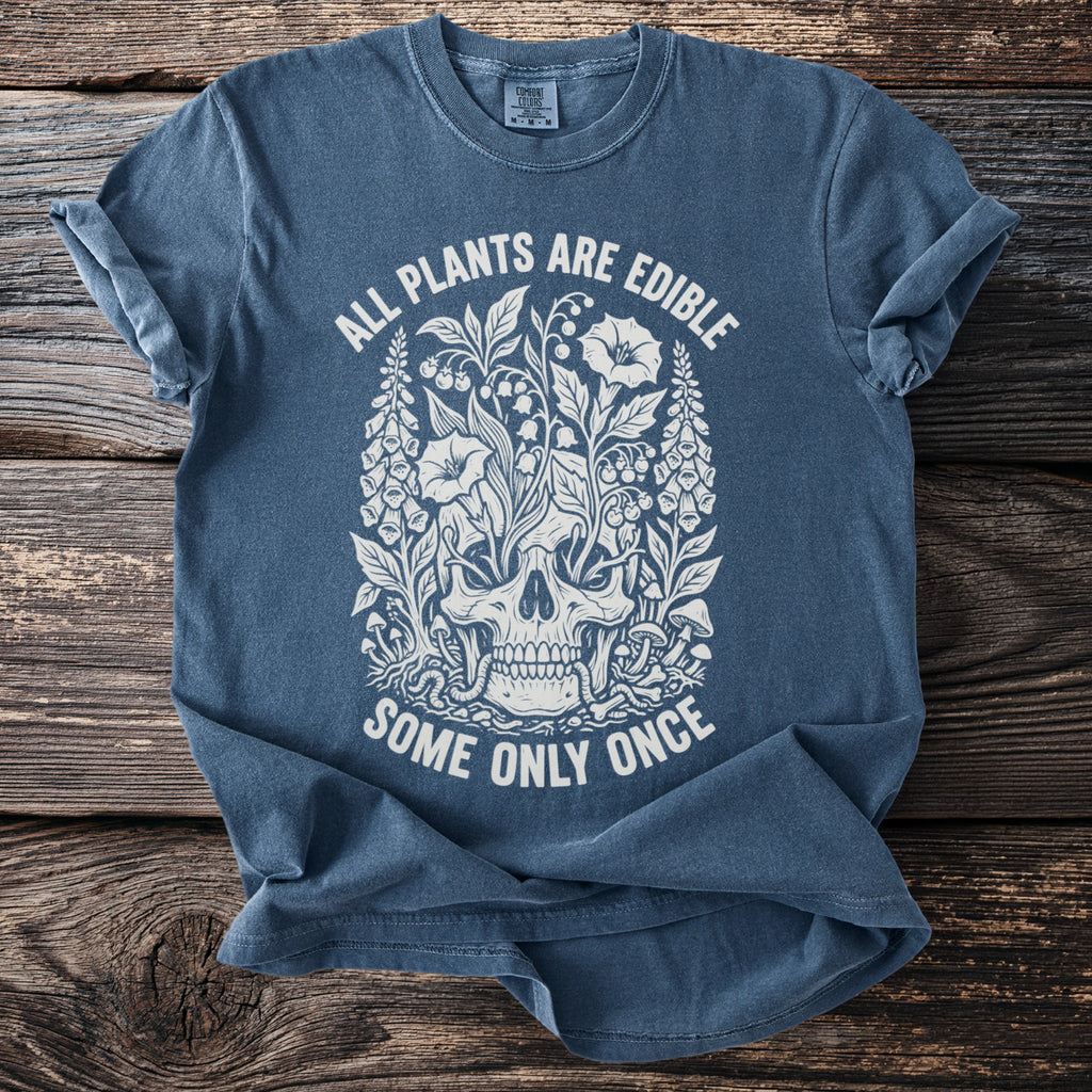 Blue t-shirt with a white graphic of a skull surrounded by plants and the text "ALL PLANTS ARE EDIBLE SOME ONLY ONCE".