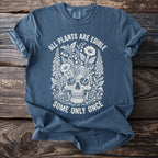 Blue t-shirt with a white graphic of a skull surrounded by plants and the text "ALL PLANTS ARE EDIBLE SOME ONLY ONCE".