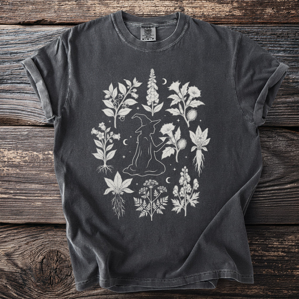 Dark grey t-shirt with white graphic of a witch surrounded by botanical illustrations.