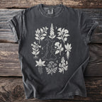 Dark grey t-shirt with white graphic of a witch surrounded by botanical illustrations.