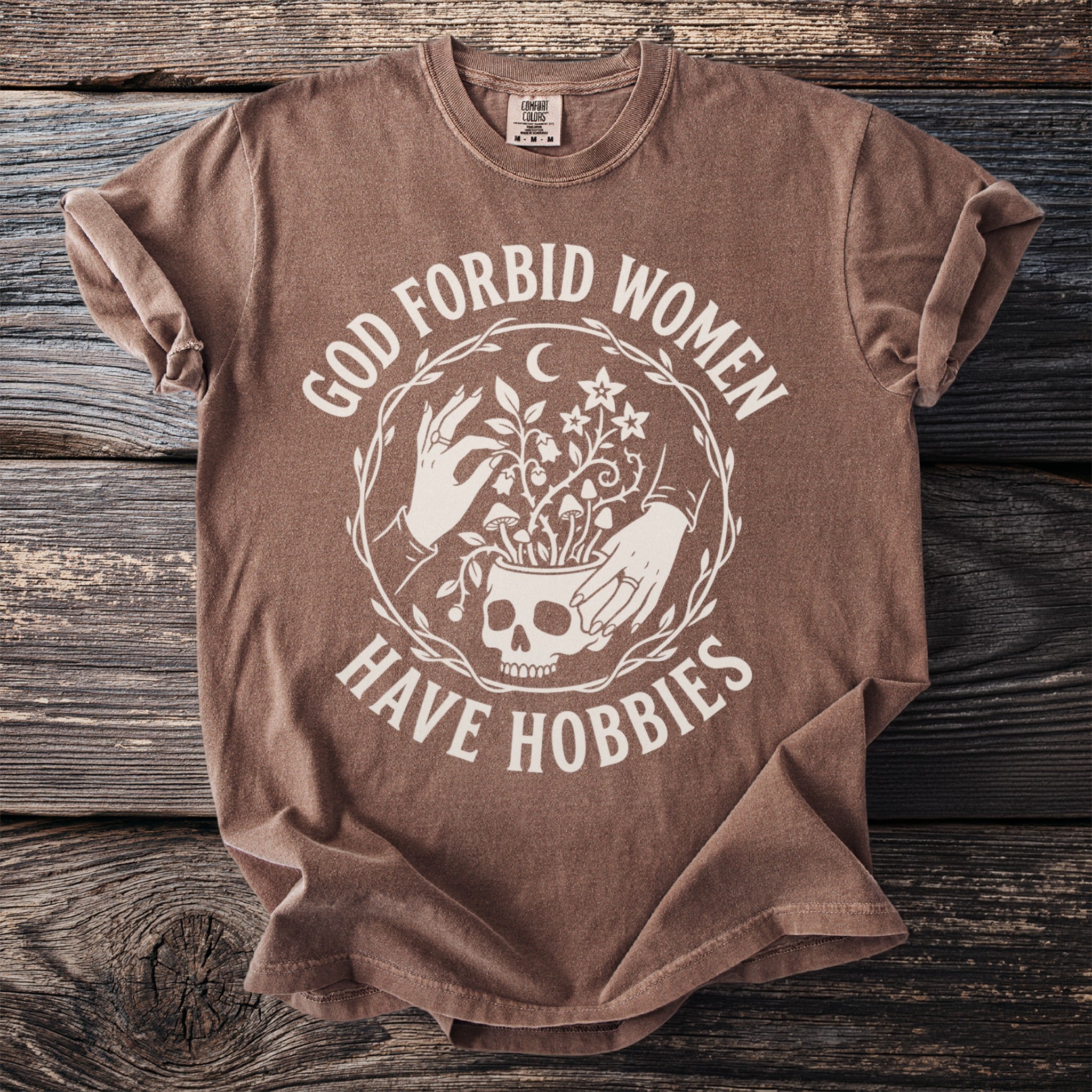 Brown t-shirt with white text and illustration of skull, hands, and plants.