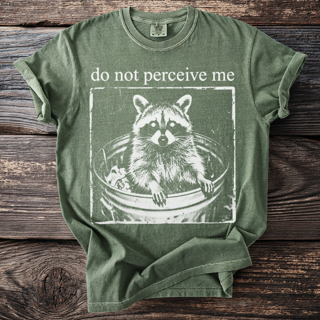 Green t-shirt with white graphic of raccoon in trash can and text "do not perceive me".
