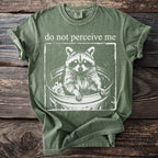 Green t-shirt with white graphic of raccoon in trash can and text "do not perceive me".