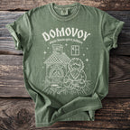 Green t-shirt with a white graphic of a Domovoy spirit sitting by a hearth.