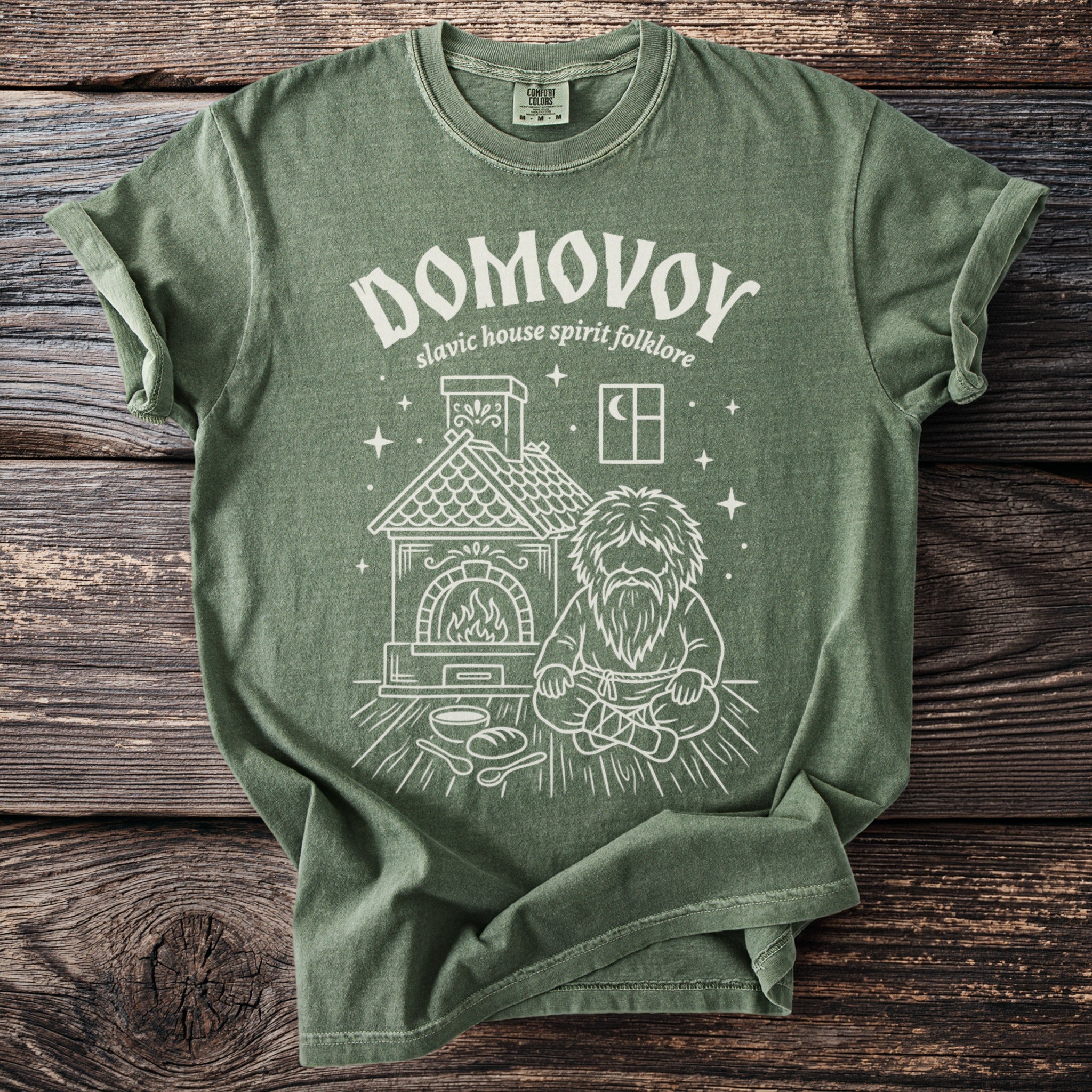 Green t-shirt with a white graphic of a Domovoy spirit sitting by a hearth.