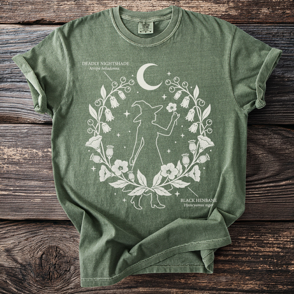 Green t-shirt with witch silhouette, crescent moon, and botanical illustrations of Deadly Nightshade and Black Henbane.