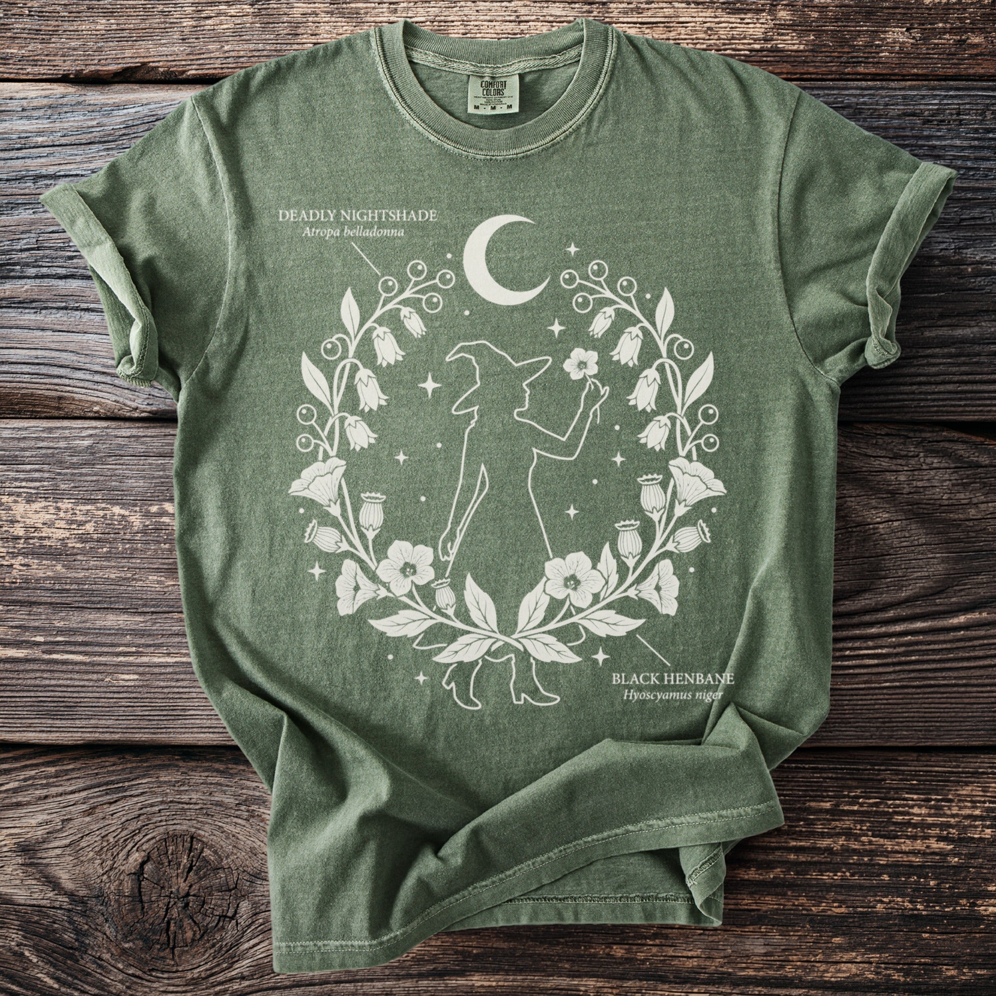 Green t-shirt with witch silhouette, crescent moon, and botanical illustrations of Deadly Nightshade and Black Henbane.