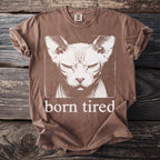 Brown t-shirt with a graphic of a grumpy hairless cat and the text "born tired".