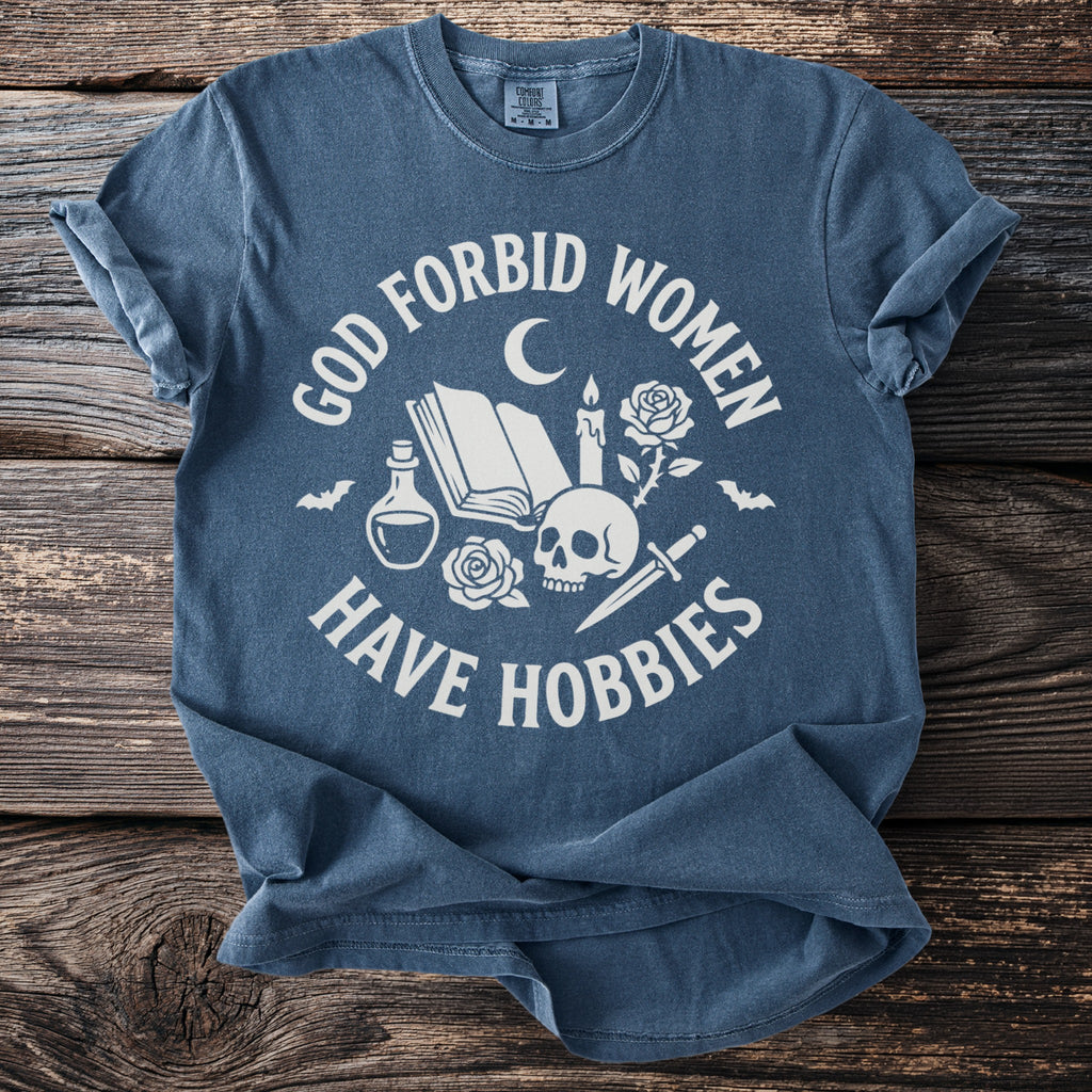 Blue t-shirt with white text "God forbid women have hobbies" and gothic symbols.
