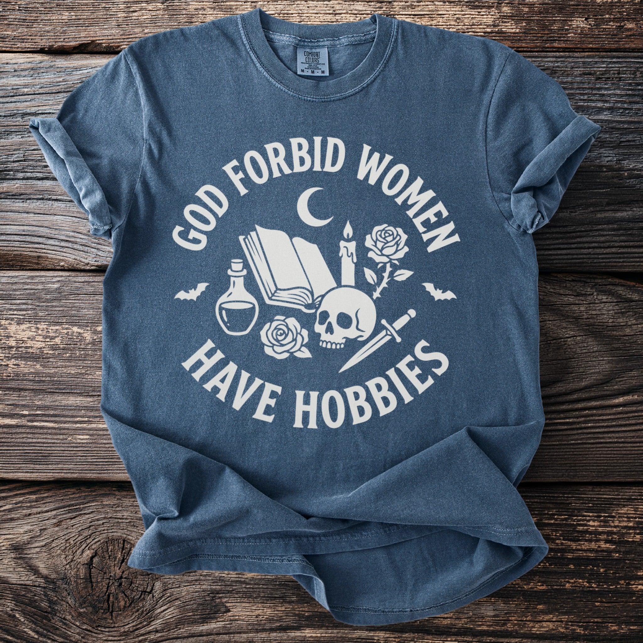 Blue t-shirt with white text "God forbid women have hobbies" and gothic symbols.