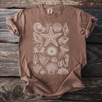 Brown t-shirt with white line drawings of assorted seashells and sea creatures.