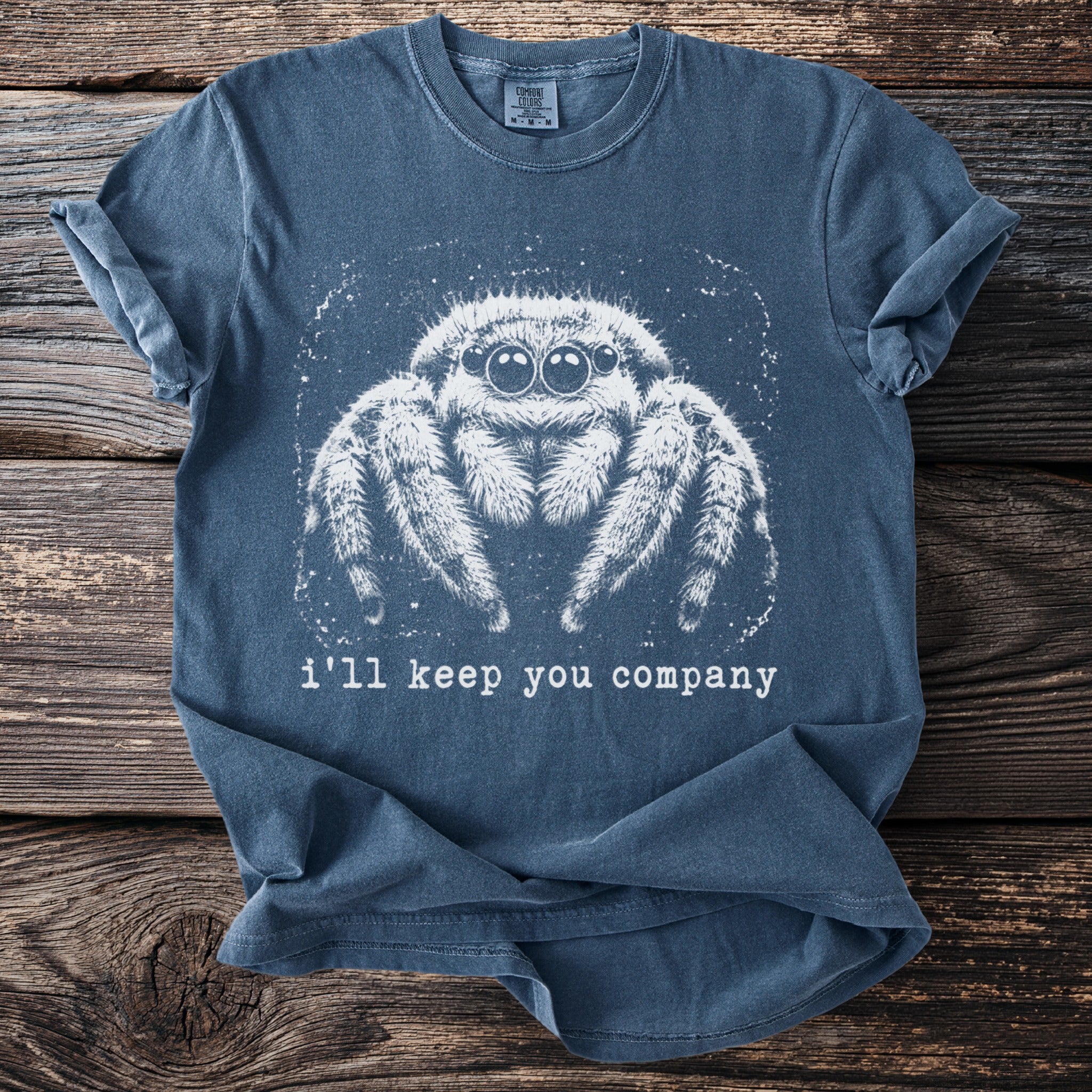 Blue t-shirt with white graphic of a jumping spider and text "i'll keep you company".