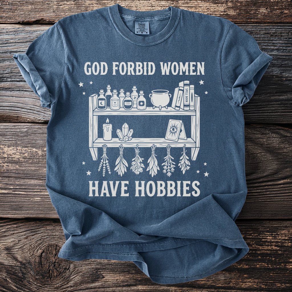 Blue t-shirt with graphic saying "God forbid women have hobbies" and witchy items.