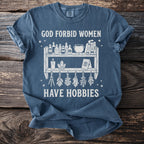Blue t-shirt with graphic saying "God forbid women have hobbies" and witchy items.