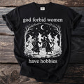 Black t-shirt with "god forbid women have hobbies" and a witch coven illustration.