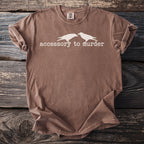 Brown t-shirt with white graphic of two birds and text "accessory to murder".