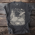 Dark grey t-shirt with the Comfort Colors tag. The graphic features a black cat, an open book, a quill, a candle, and mushrooms.