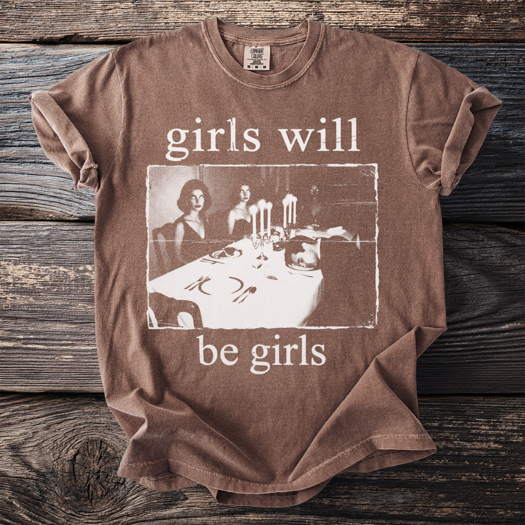 Brown t-shirt with "girls will be girls" text and vintage image of a formal dinner.