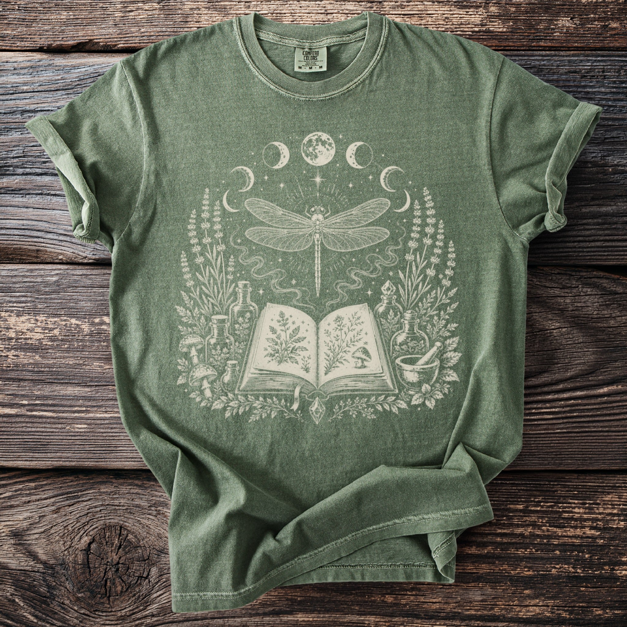 Green t-shirt with a celestial dragonfly, open book, and botanical illustrations.