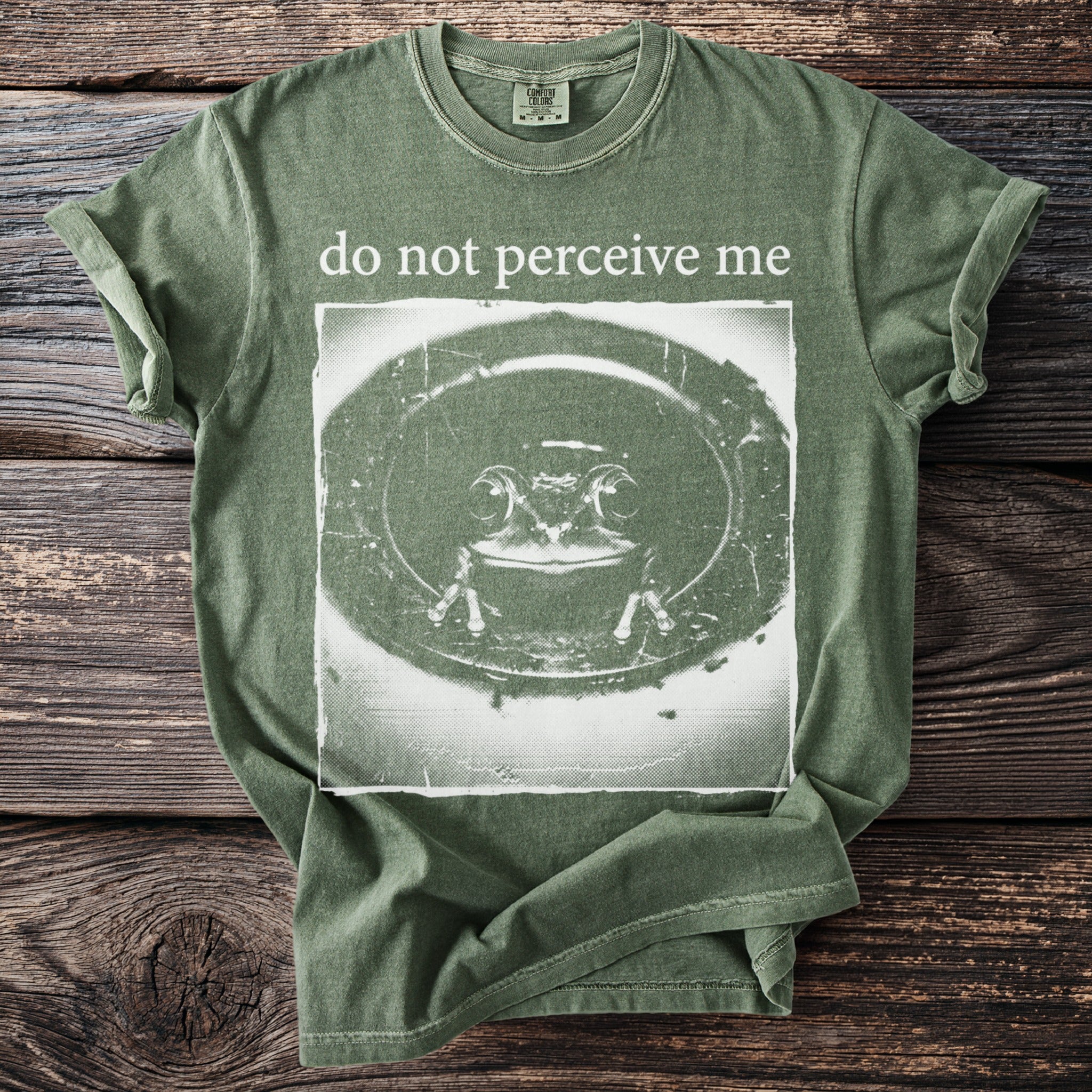 Green t-shirt with "do not perceive me" and a distressed frog graphic.