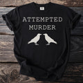 Black t-shirt with "ATTEMPTED MURDER" text and two white crow silhouettes.