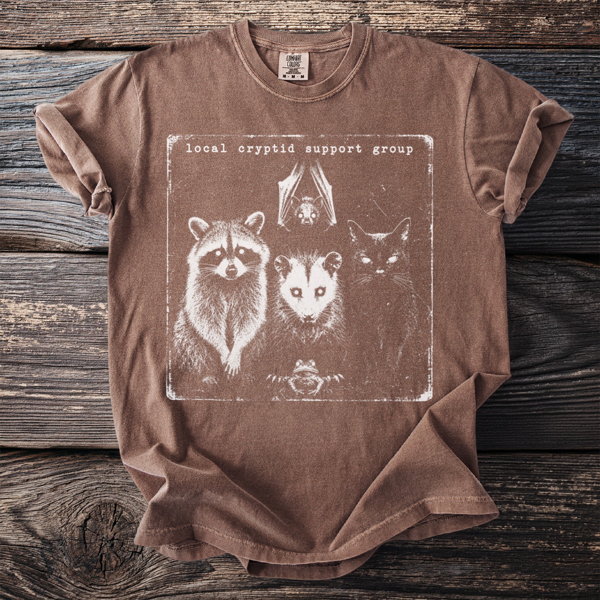 Brown t-shirt with graphic of bat, raccoon, opossum, cat, and frog.