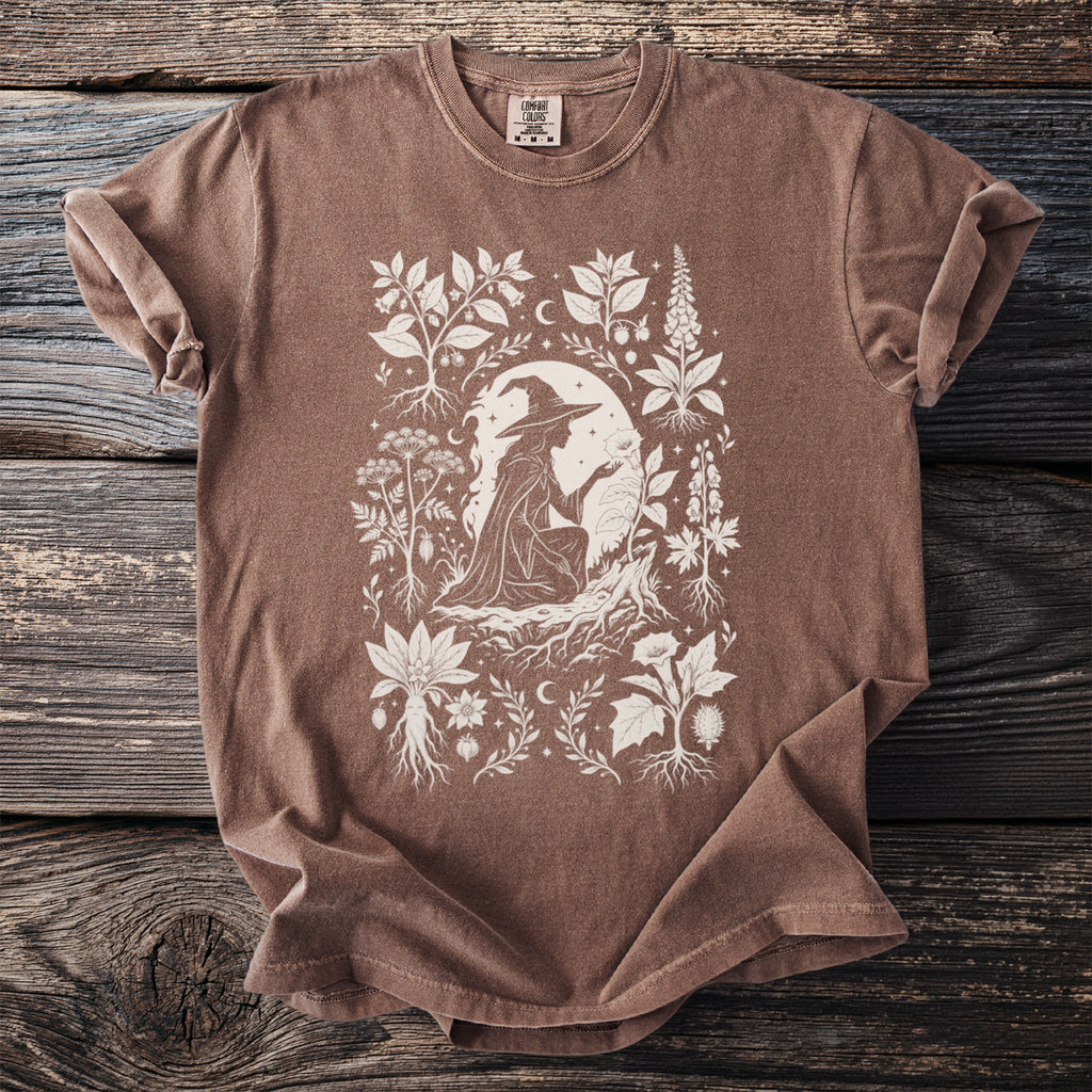 Brown t-shirt with a white line drawing of a witch and botanical elements.