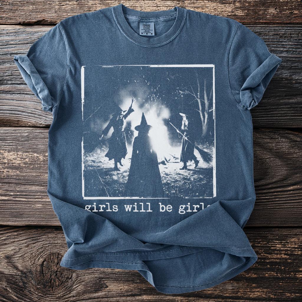Blue shirt with three witches around a bonfire and text "girls will be girls".