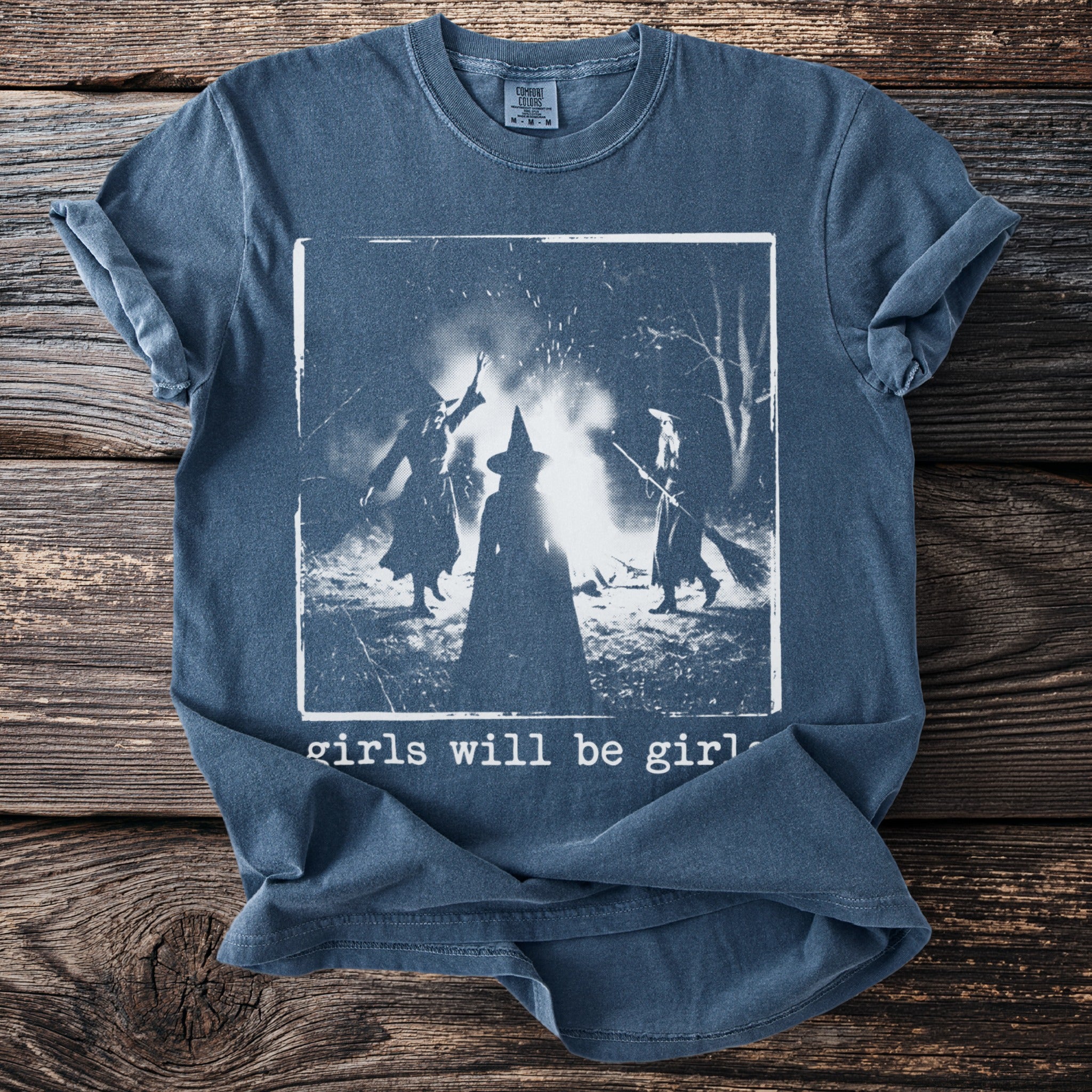 Blue shirt with three witches around a bonfire and text "girls will be girls".