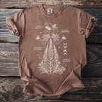 Brown t-shirt with white line art of a witch and plants, labeled "Taxus Baccata," "Digitalis Purpurea," and "Ricinus Communis."