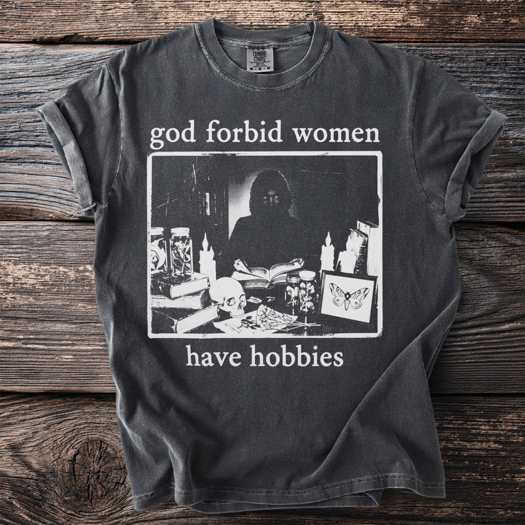 Dark gray t-shirt with the text "god forbid women have hobbies" and a dark framed graphic.