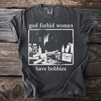 Dark gray t-shirt with the text "god forbid women have hobbies" and a dark framed graphic.